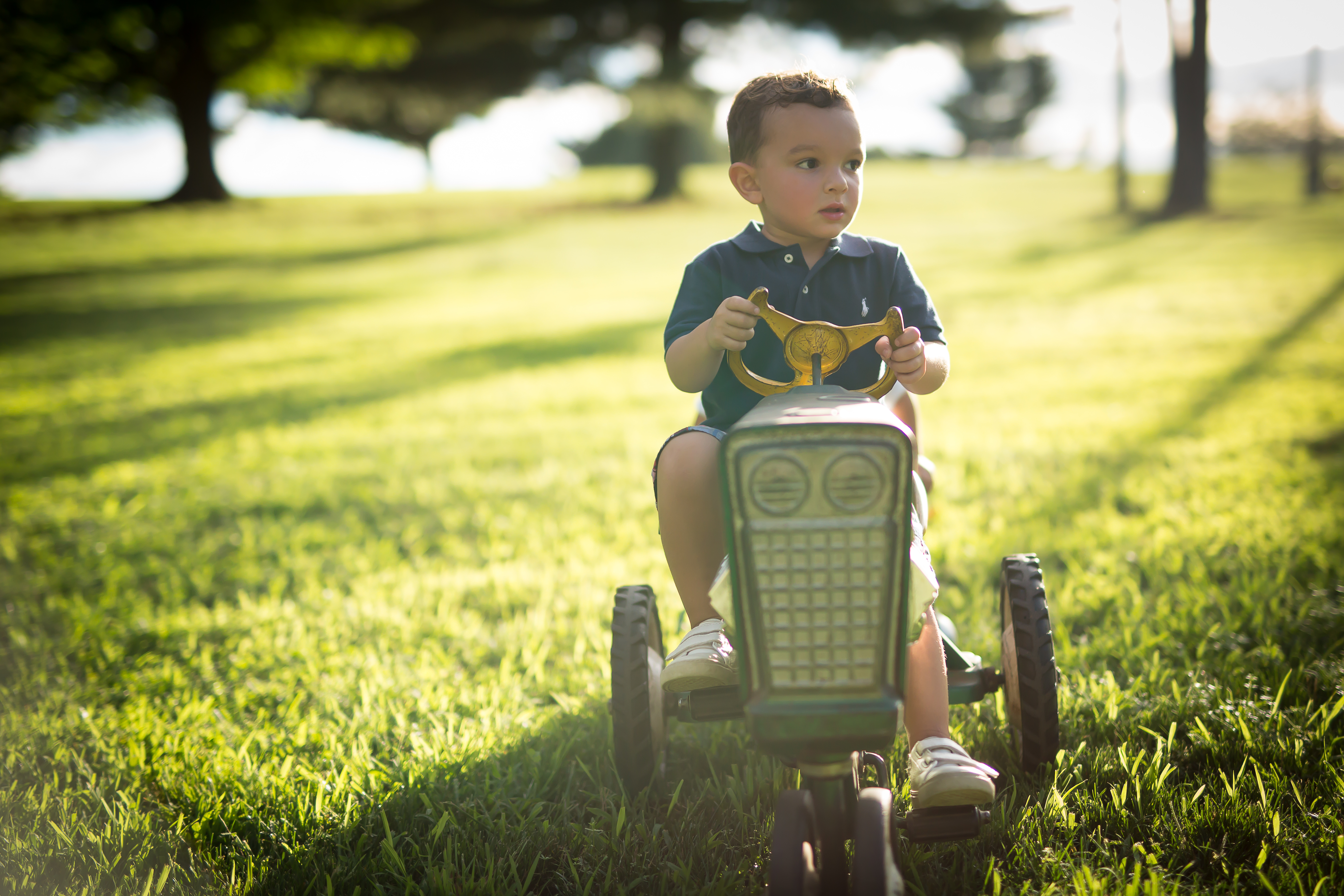 what time of day is best for your photo shoot? Little boy on a toy tractor, on a grassy hill. Late afternoon sun is streaming down on the grass.
