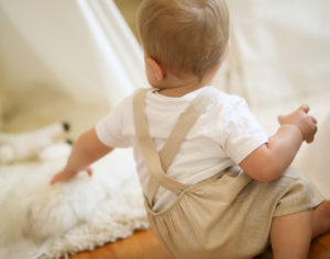 studio wardrobe: baby sitting on the ground in beige overall shorts.