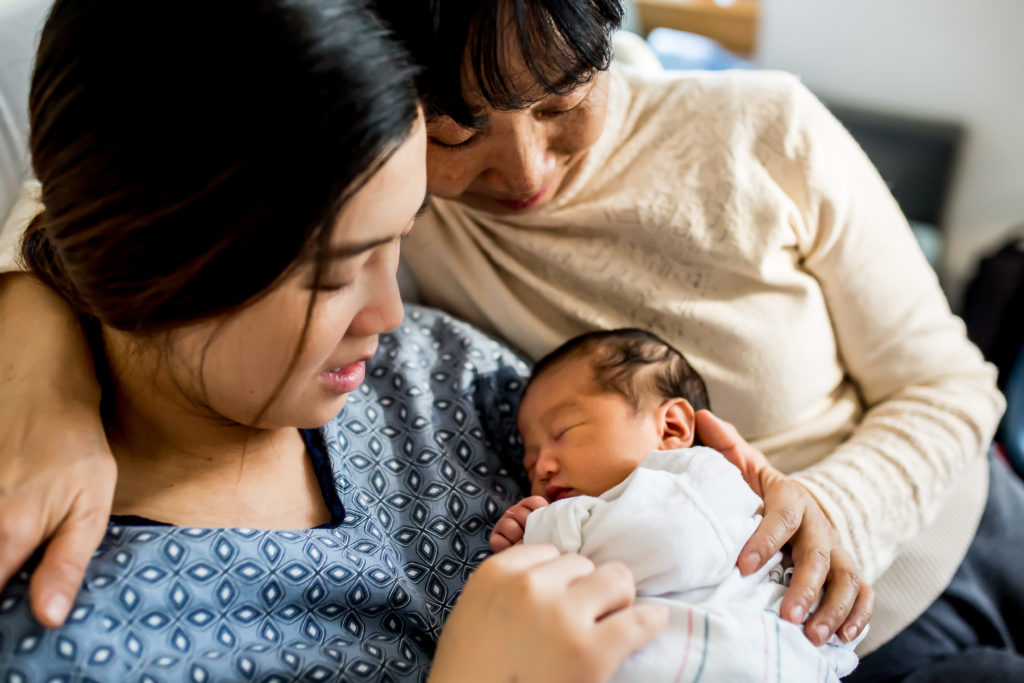 newborn baby being held by his mother, with his grandmother hugging them. In the hospital, newborn session.