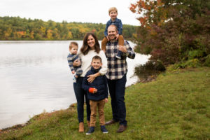 Great family photo location! family with 3 boys stands together, next to Lake Waban, in Wellesley, MA. Fall colors in trees in background