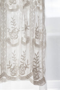 studio wardrobe: detail of white lace long gown, with embroidered flowers, hanging in front of window.