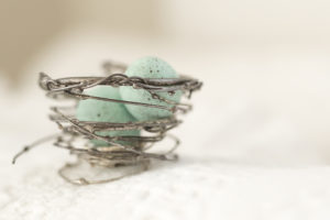 tiny wire nest and blue eggs inside. decorative item, sitting on a white blanket.