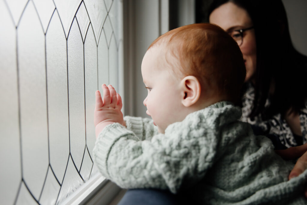 Beth Cuddy Photography family photographer baby touching window, with good light on face.
