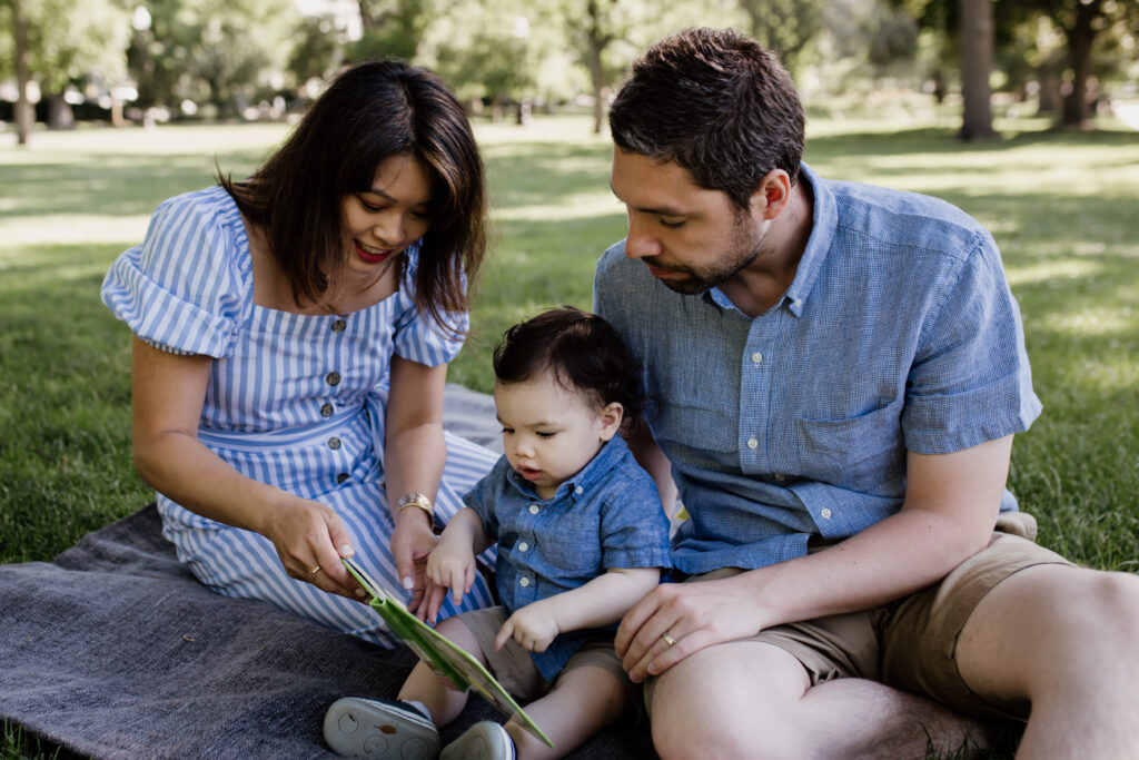 summer family photo of couple reading to their baby on the grass
